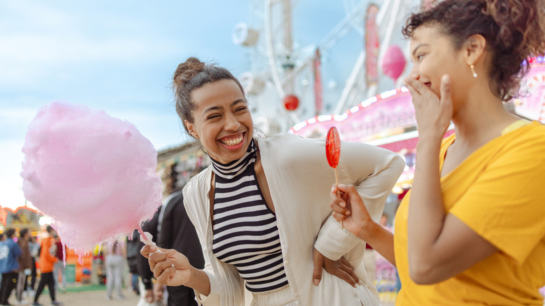 Two people laughing and enjoying cotton candy and a lollipop at the fair