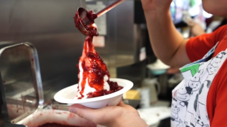 Unidentified person pouring berry syrup over ice cream sundae