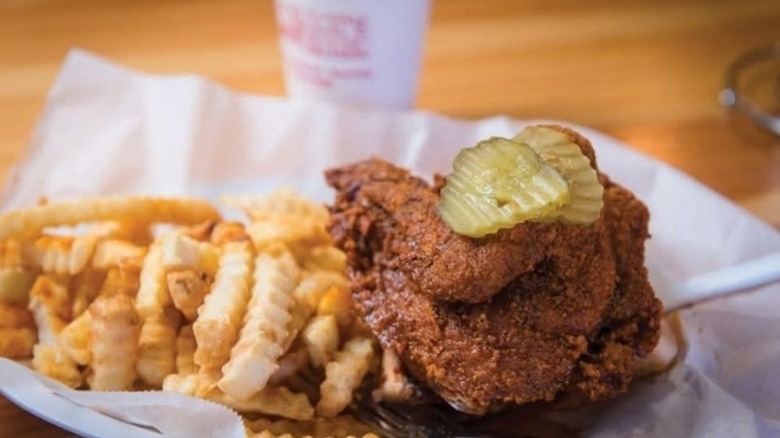 Hot fried chicken with pickles and fries on plate