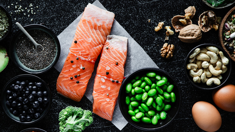 Salmon sitting on a piece of tissue surrounded by nuts, capers, broccoli and legumes. There are peppercorns and salt flakes on top of the salmon