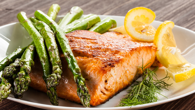 cooked grilled salmon on plate with asparagus and lemon slices and dill