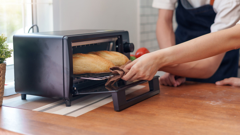 close up of someone pulling bread from black toaster oven on wood counter