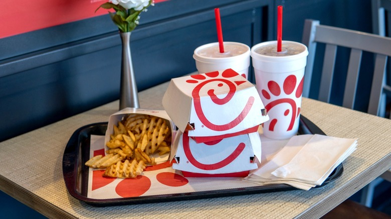 Chick-fil-A sandwich boxes, two soft drink cups, napkins, and a sleeve of waffle fries on black tray sitting on table