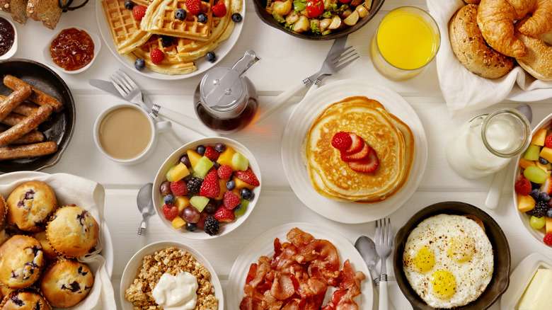 A variety of breakfast foods: pancakes, fruit, bacon, granola, pastries, sausage, juice, coffee