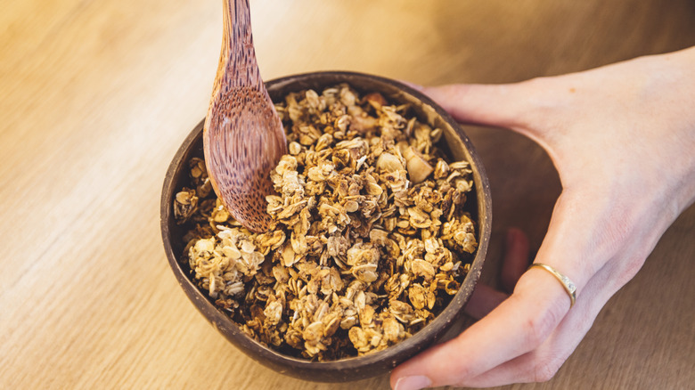 A person holds a bowl of granola, mixed with wooden spoon