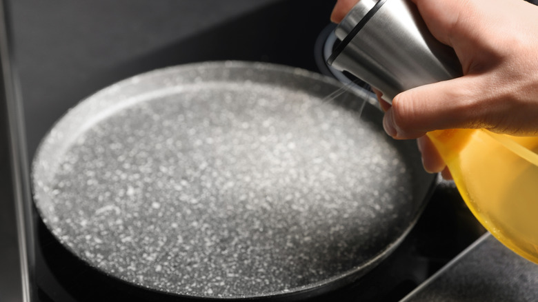 close up of person using spray olive oil on stovetop pan