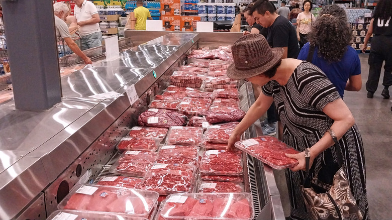 Woman shopping for beef in a larger meat display cooler at Costco