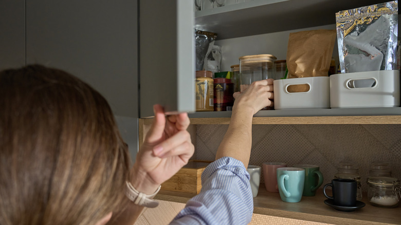 Woman reaching onto kitchen shelves with organized containers