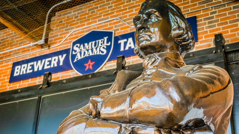 Statue of Sam Adams in front of brick wall and brewery sign