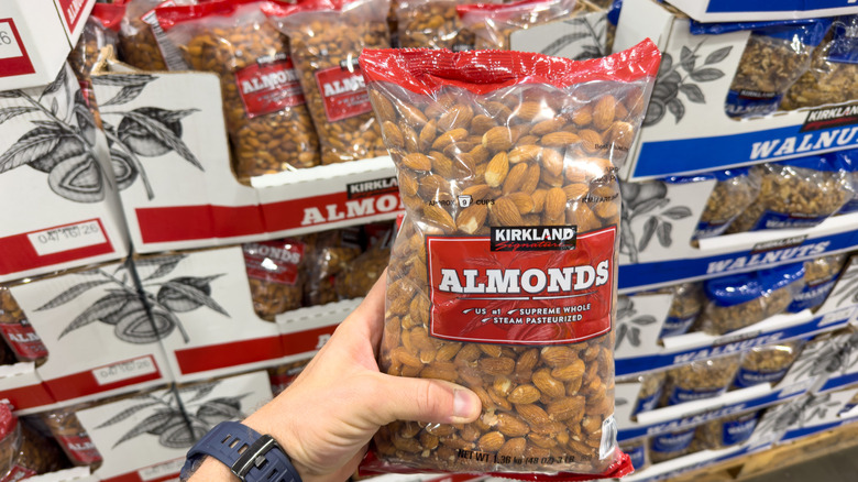 someone holding up a Kirkland brand bag of almonds in front of the store display with the walnuts in the background too