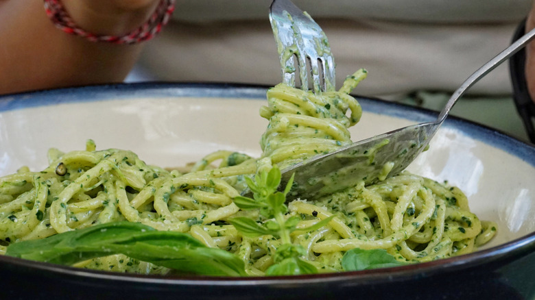 A person stirs winds noodles with pesto around a fork with a spoon