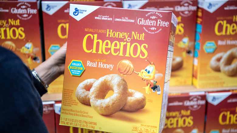 A person holds a box of Honey Nut Cheerios box in a store.