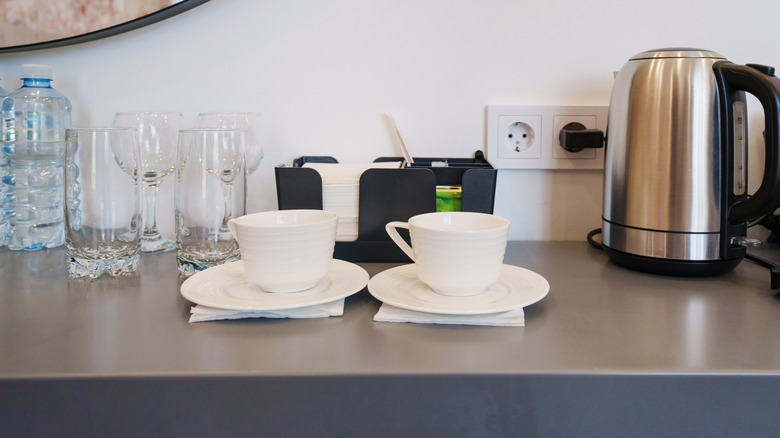 teacups, electric kettle, glasses, and napkins on hotel room bar