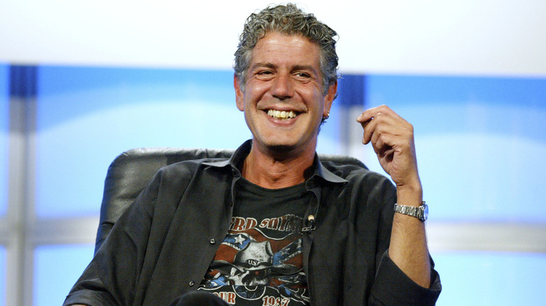 Anthony Bourdain in a black button down shirt over a t-shirt, smiling
