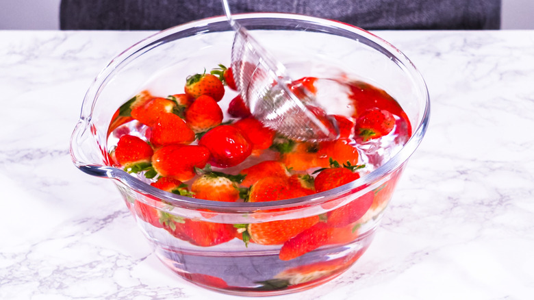 strawberries soaking in water in a glass bowl