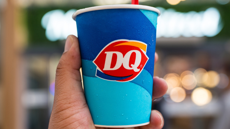 A hand holding a blue Dairy Queen branded cup with a red spoon sticking out of the top