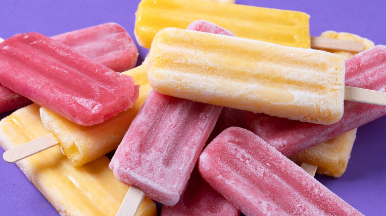 Red strawberry popsicles and yellow popsicles on purple background