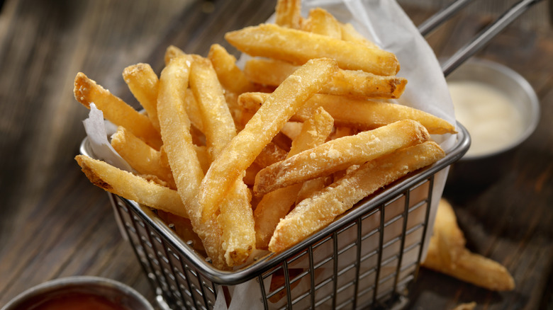A closeup of a basket of french fries with dipping sauces in the background