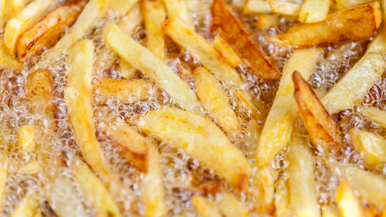 A closeup of golden french fries frying in hot oil