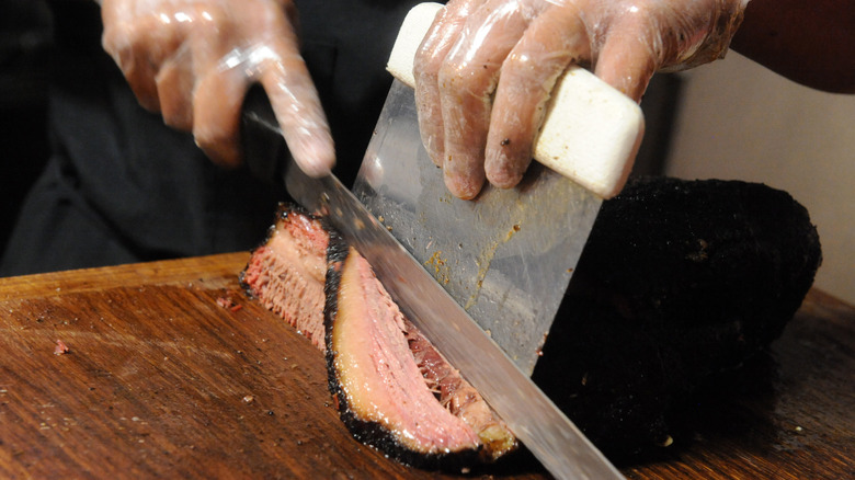 Hand slicing brisket on wooden cutting board
