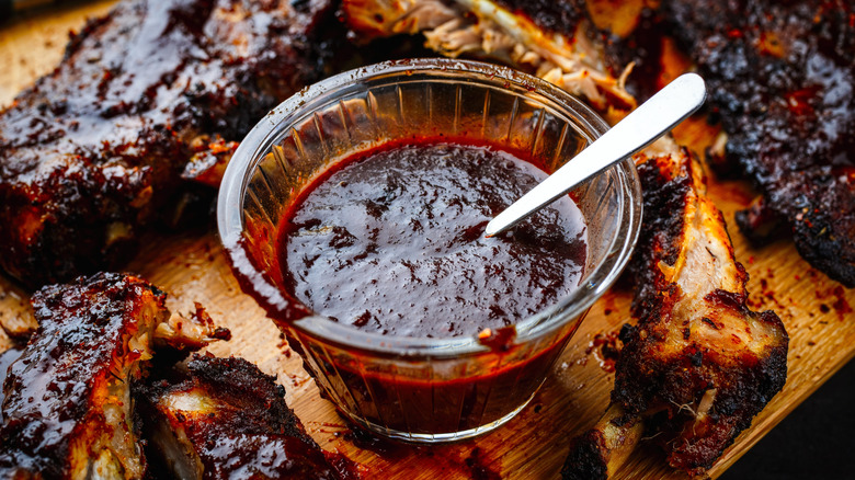 A bowl of barbecue sauce on a cutting board with ribs
