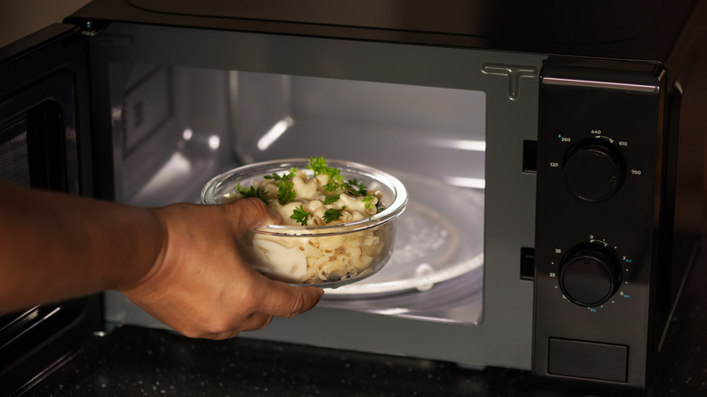 Person microwaving a container of macaroni