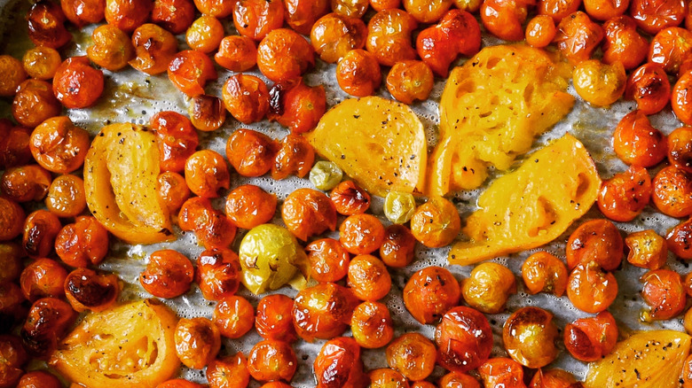 A tray of bright red blistered cherry tomatoes with some larger sliced yellow tomatoes scatters throughout