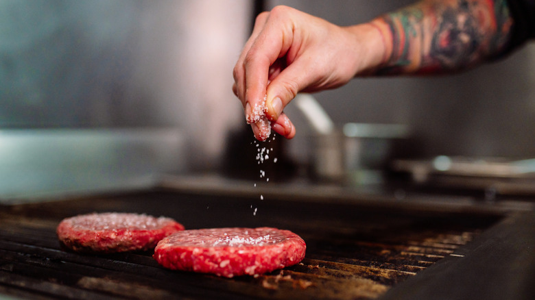 Cook salting raw burgers on the grill