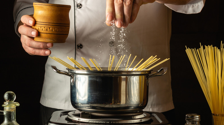 Person adding salt to boiling pasta water