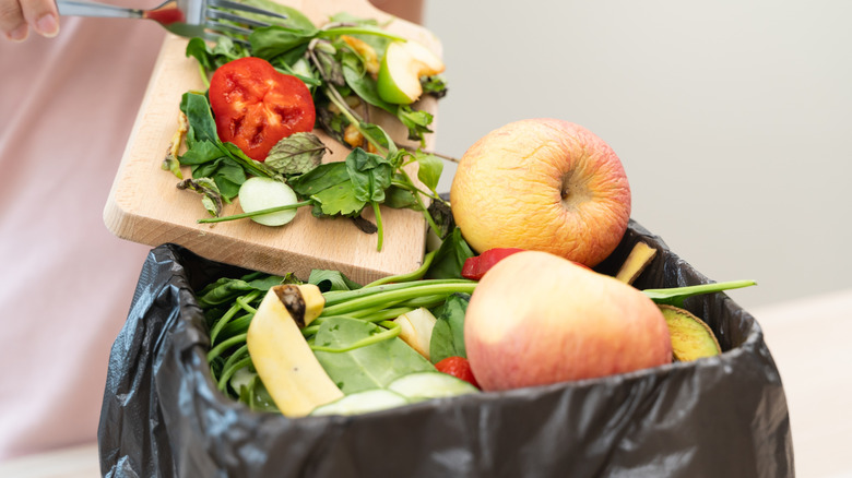 Person pushing spoiled produce into lined garbage can