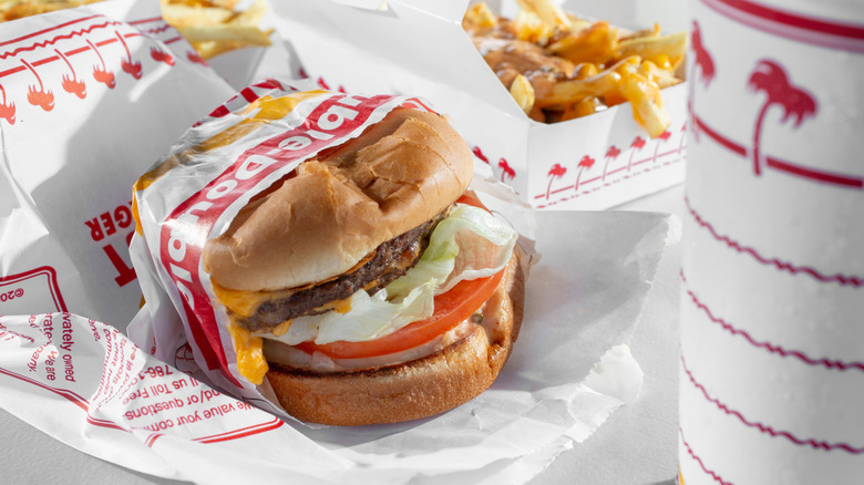 An In-N-Out burger in a wrapper, with fries in the background