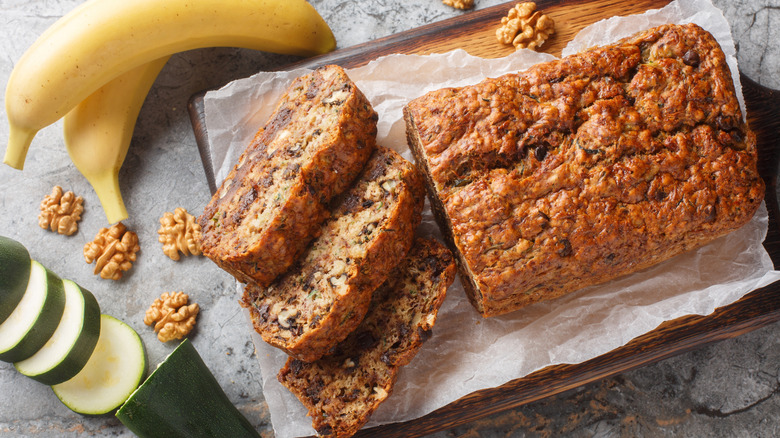 Banana bread on a pan surrounded by bananas and zucchini