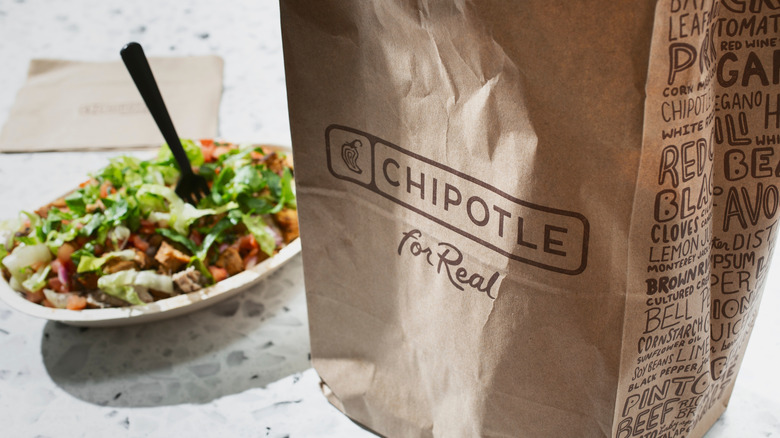 Paper Chipotle bag on a white stone countertop with a burrito bowl out of focus behind it