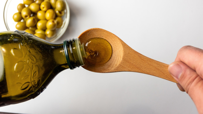 Person pouring olive oil onto a wooden spoon