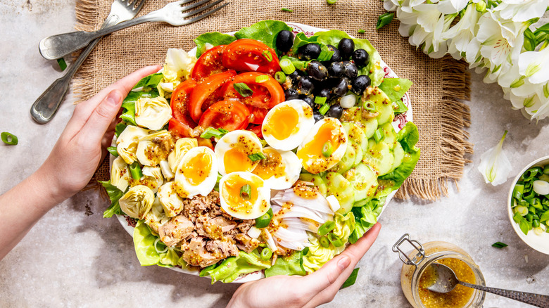 Niçoise salad on a large plate featuring lettuce, tomatoes, eggs, cucumbers, and black olives