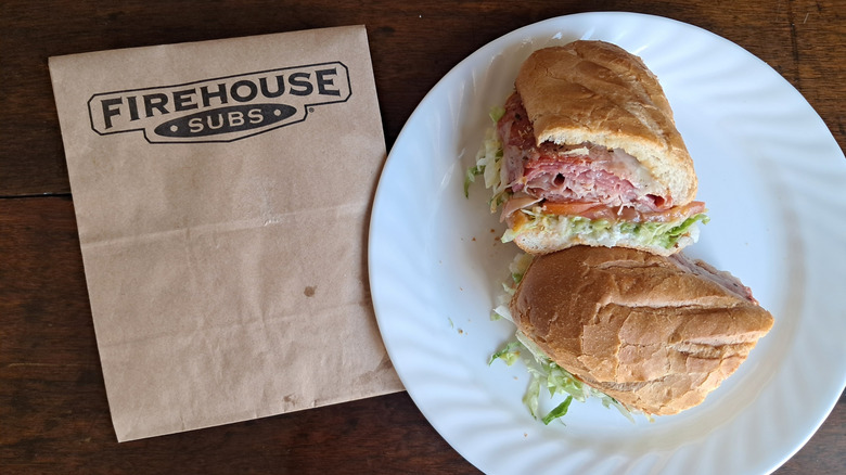 Firehouse Subs sandwich cut in half on a plate next to a Firehouse Subs bag.