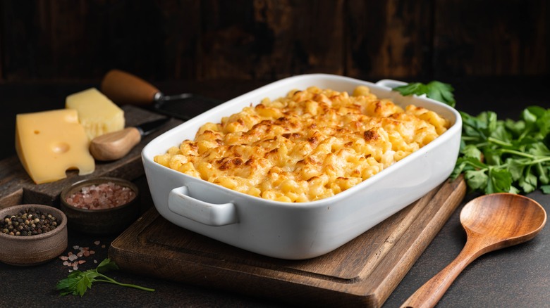 mac and cheese in a white casserole dish on wood board