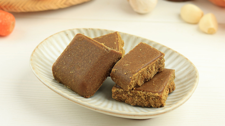 Japanese curry cubes on a small ceramic plate with garlic and carrots in the background
