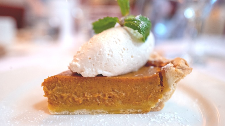 Slice of pumpkin pie with scoop of cream topping on white plate