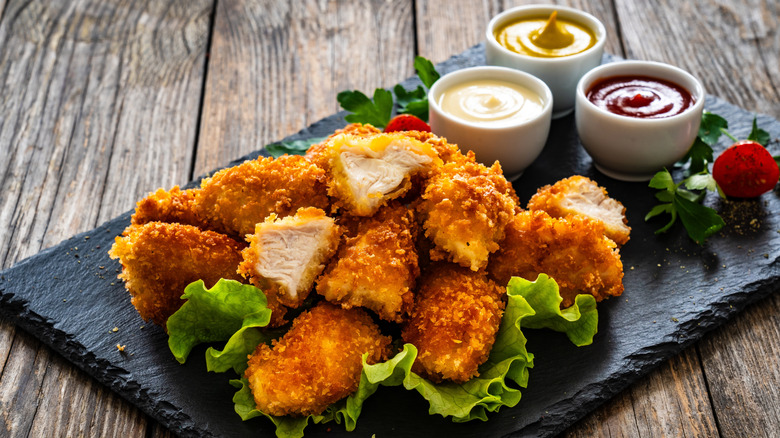 Breaded chicken nuggets on a board next to white bowls of condiments