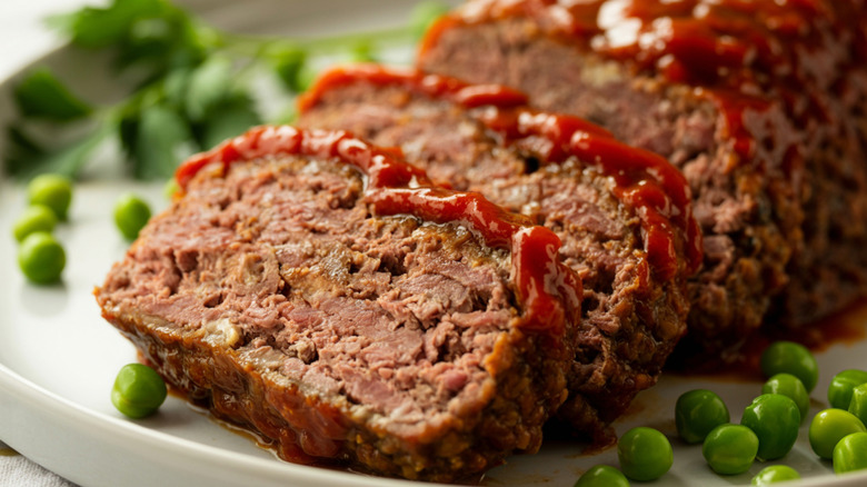A sliced meatloaf with a ketchup glaze on a plate with peas