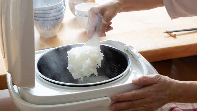 Person scooping steaming rice from rice cooker