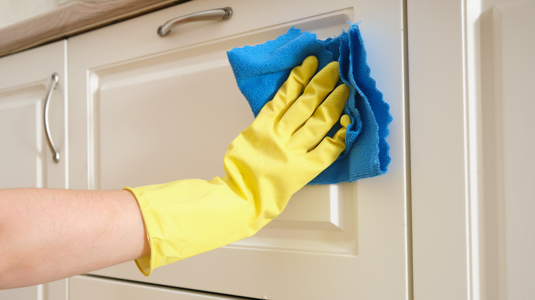 person cleaning kitchen cabinets while wearing yellow rubber gloves
