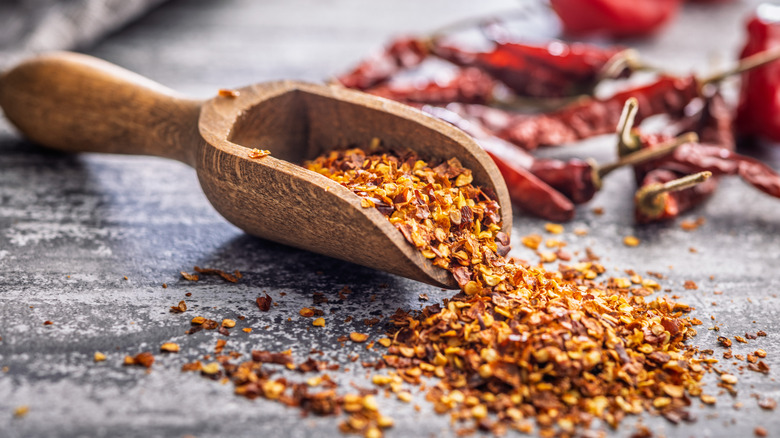 A wooden scoop of red pepper flakes spilling out onto a table top