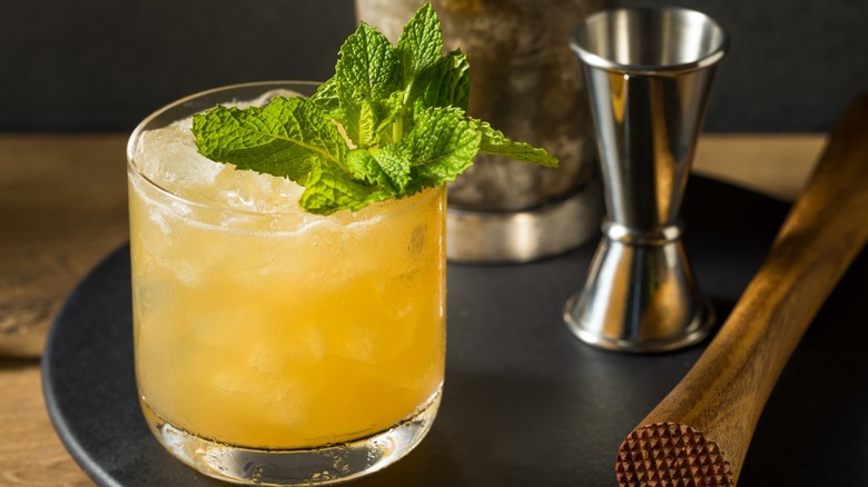 A whiskey smash with mint next to a muddler