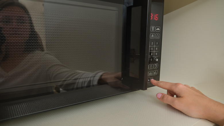 Hand pressing buttons on microwave