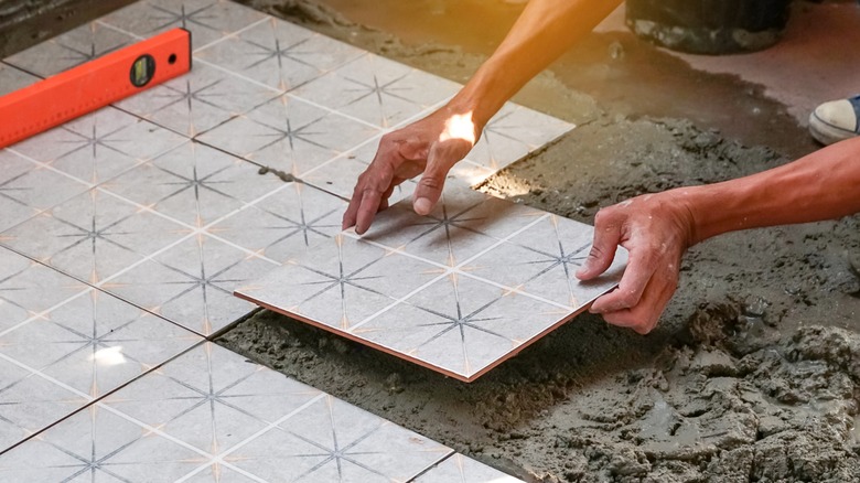 Hands installing floor tiles with grout and a level