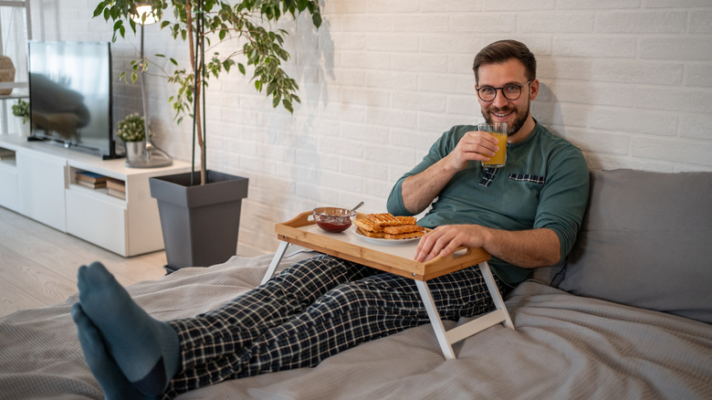 Man sipping orange juice and eating from TV tray