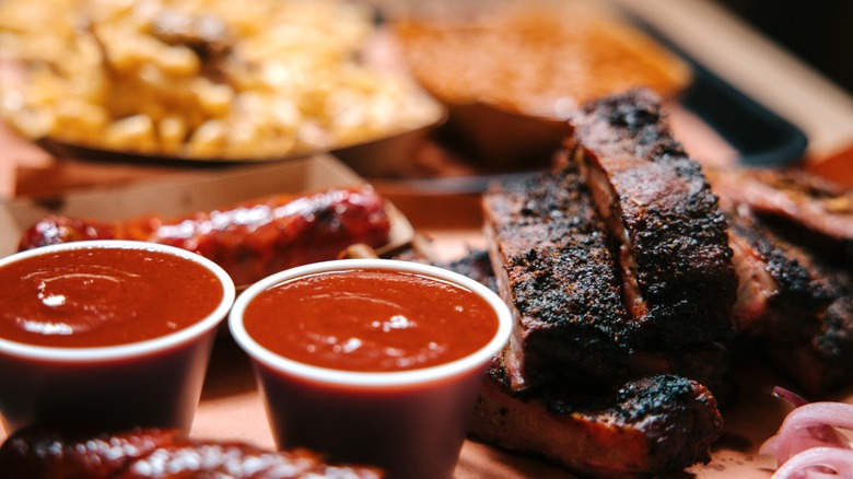 various barbecued meats with some sauces and out of focus side dishes in the background