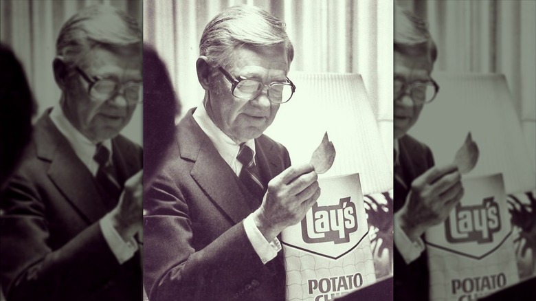 Herman Lay founder of Lay's potato chips holding a chip and chip bag.